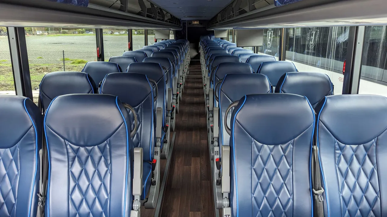56 Passenger Motorcoach interior with passenger seat belts and overhead parcel racks, photo 3 for charter bus rental